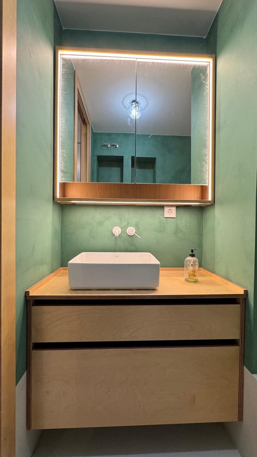 Baño en verde con mueble de lavabo en madera y espejo con luz integrada, reforma VAGAM2000.