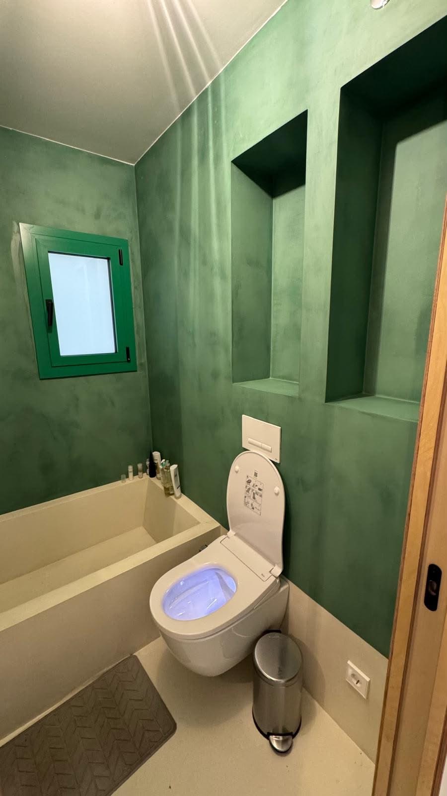 Baño con paredes verdes, ventana de carpintería verde, hornacinas y bañera de obra.