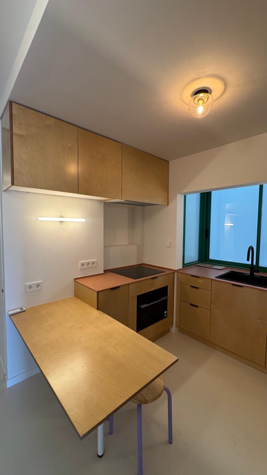 Cocina con muebles de madera clara, encimera en tono terracota y barra de desayuno, reforma VAGAM2000.