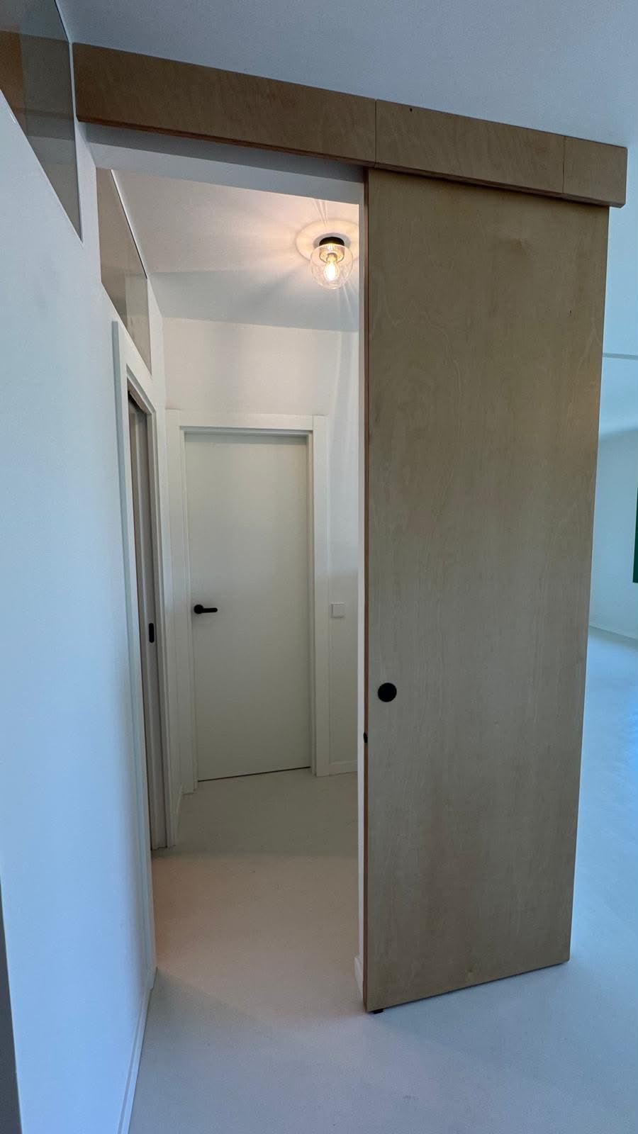 Pasillo distribuidor con puerta corredera de madera y puertas blancas con tirador negro.