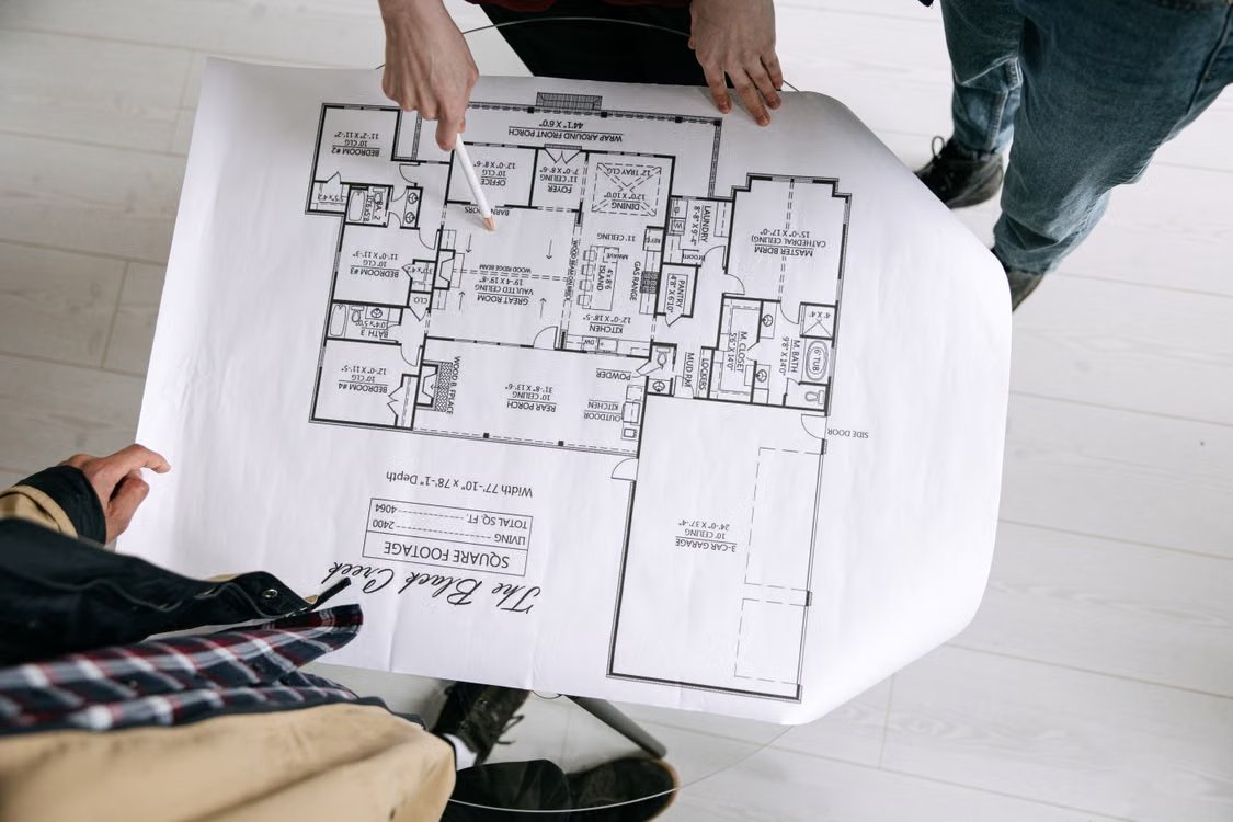 Tres personas revisando sobre una mesa el plano de una vivienda impreso en papel.