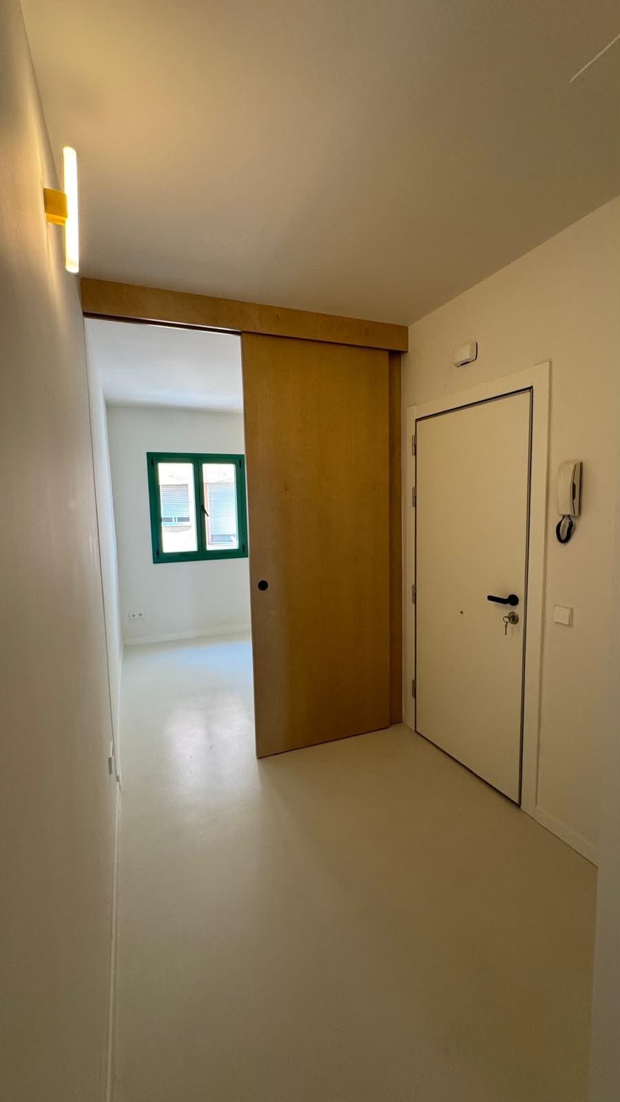 Recibidor con puerta corredera de madera que da paso a una habitación con ventana verde.