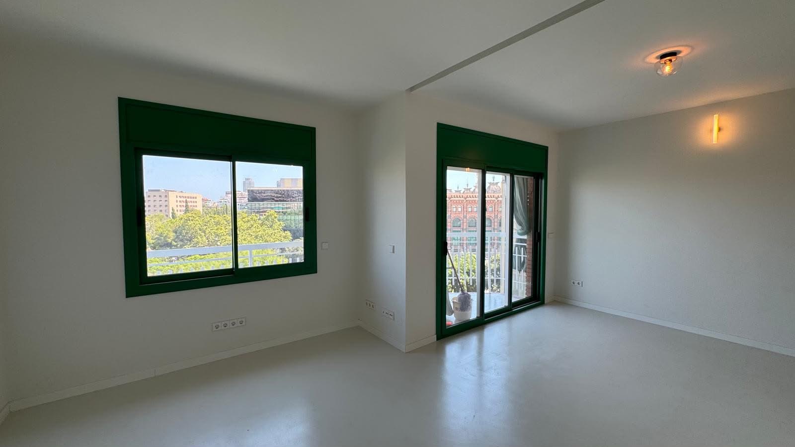 Salón luminoso con carpintería verde y suelo continuo claro, reforma VAGAM2000.